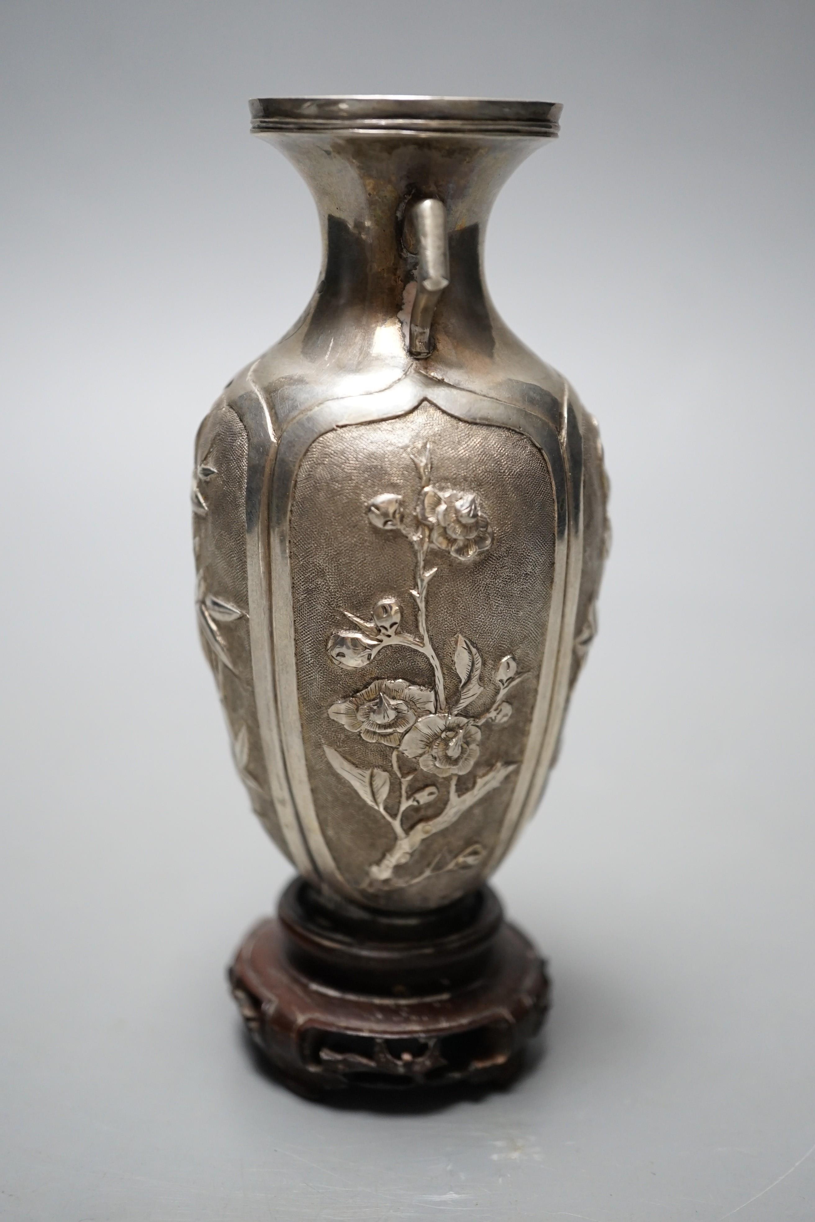 A late 19th/early 20th century Chinese Export white metal two handled vase, decorated with bamboo, peonies and prunus, on hardwood stand with white metal wing nut signed Zee Wo, vase 12cm.